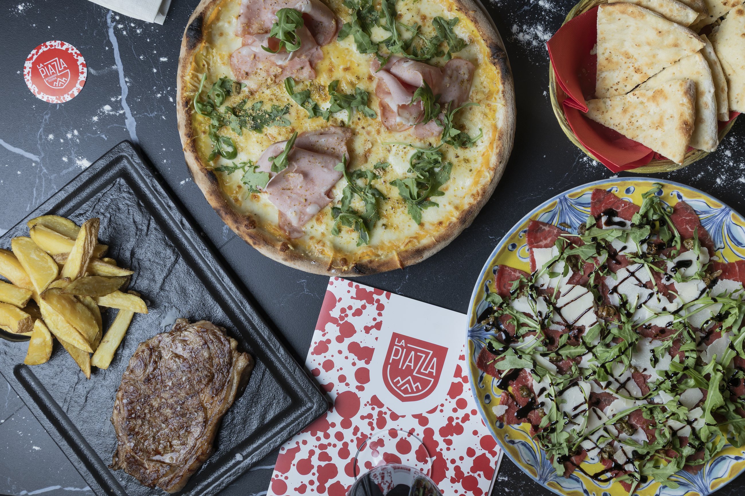 Mesa de La Piazza con pizza, carpaccio y entrecot